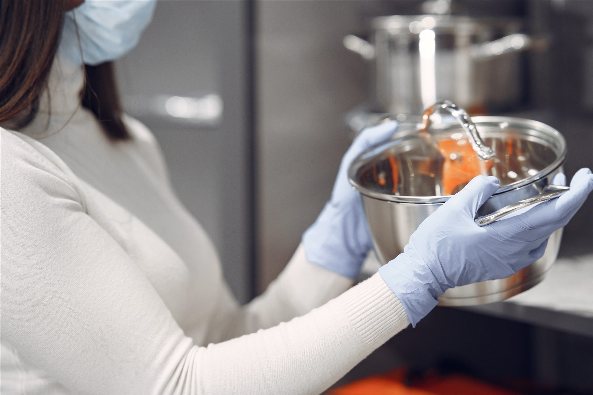 Gloved food-service worker handling clean stainless cookware